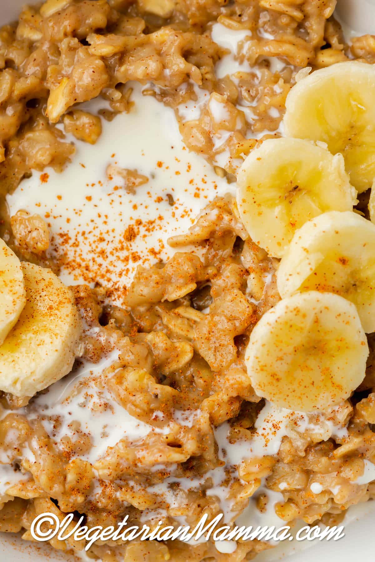 close up of white bowl with golden brown oats with some white milk. Yellow sliced bananas on top