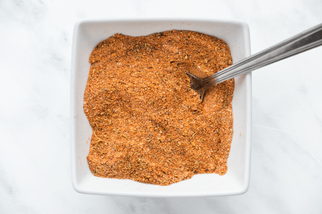 orange spices in a white square bowl with a silver spoon