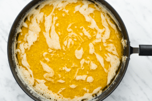 yellow and white liquid blended together in a black sauce pan