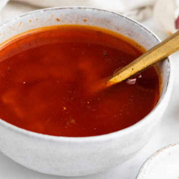 red color liquid in a white bowl with a gold spoon in it. White marble background with yellow and red spices