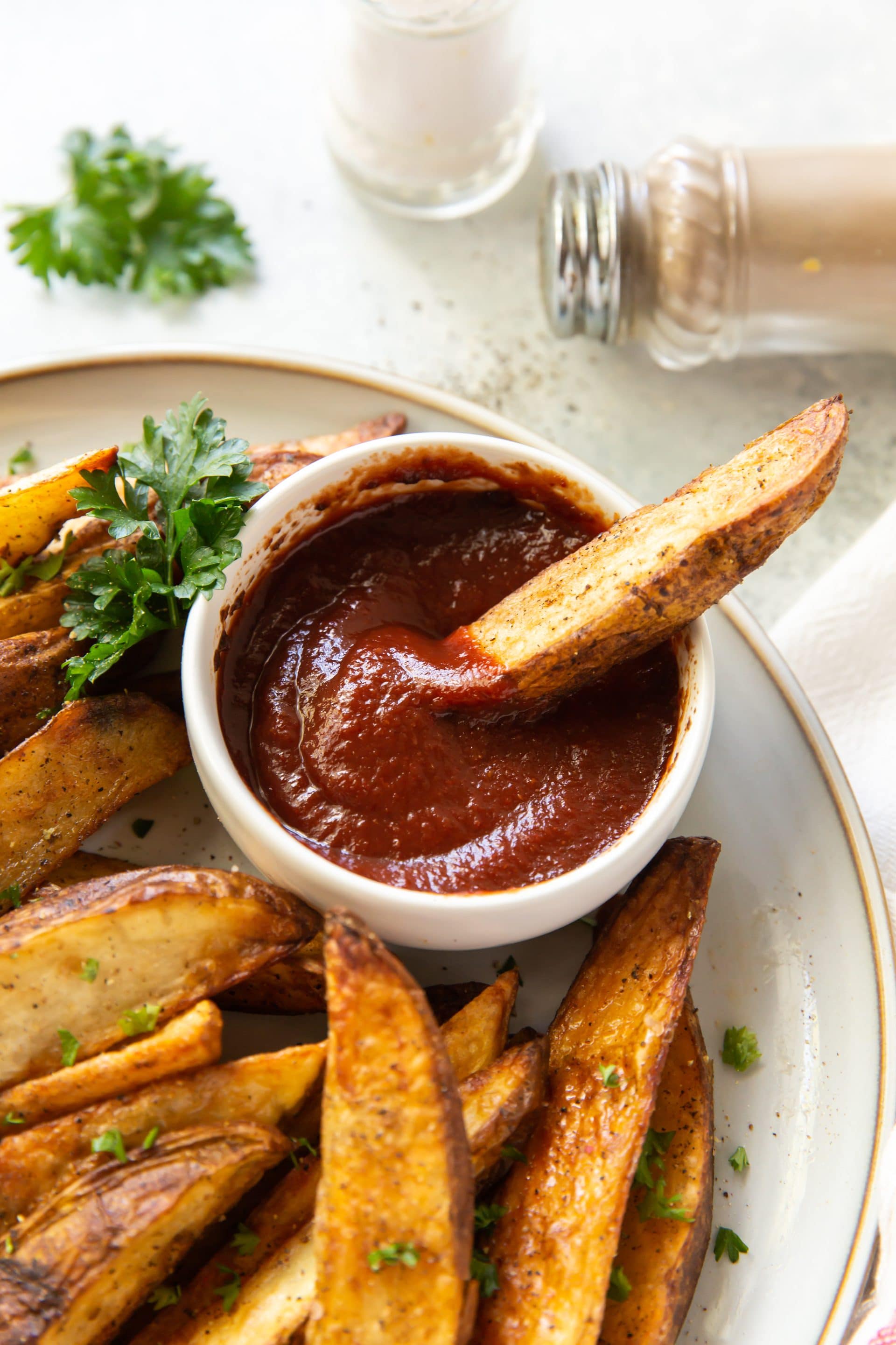 a plate of seasoned, cooked potato wedges with a side cup of ketchup., dipping fry into ketchup
