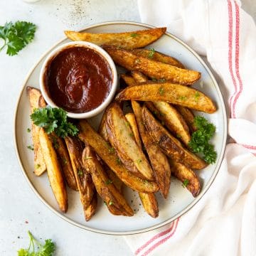 a plate of seasoned, cooked potato wedges with a side cup of ketchup.