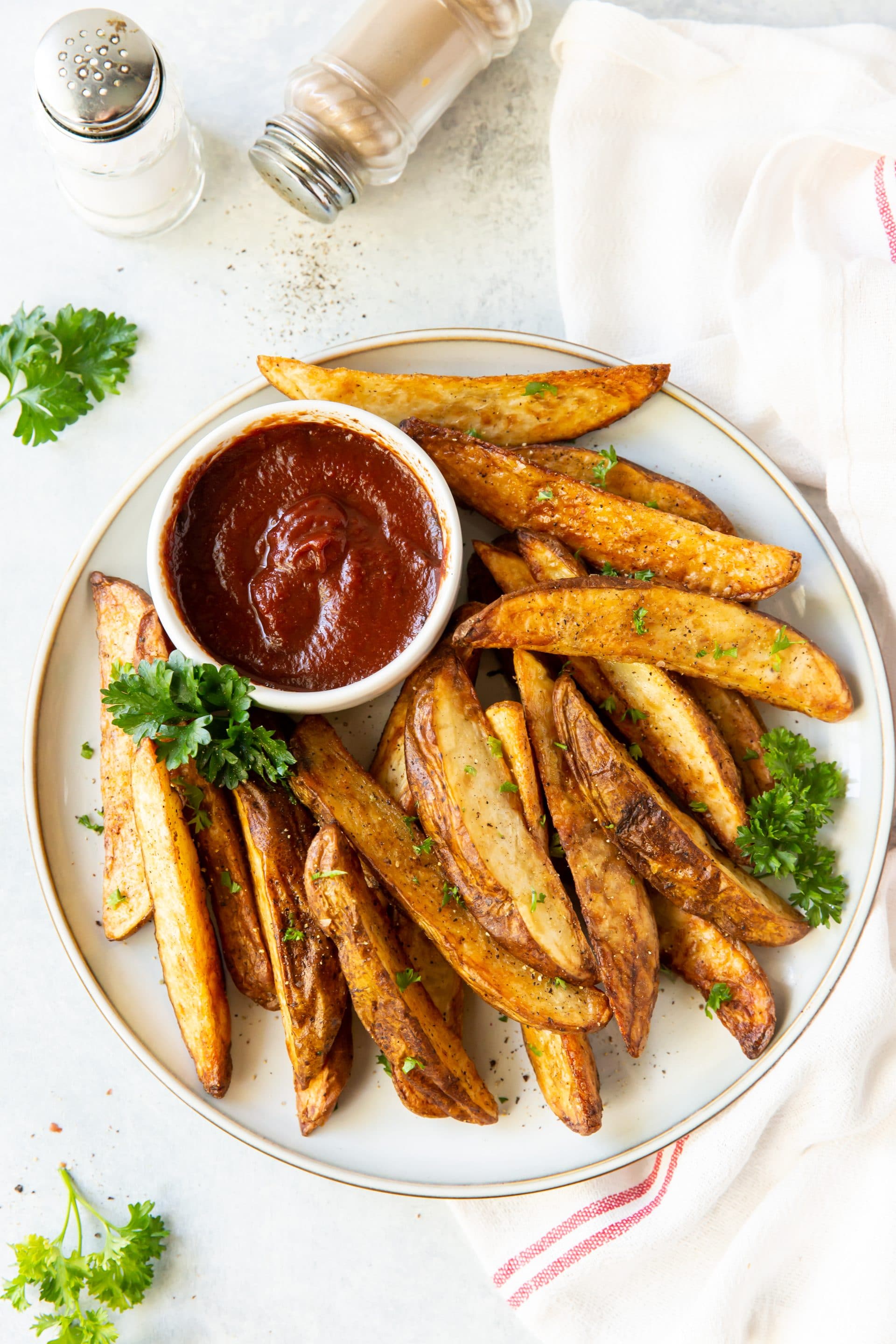 a plate of seasoned, cooked potato wedges with a side cup of ketchup.