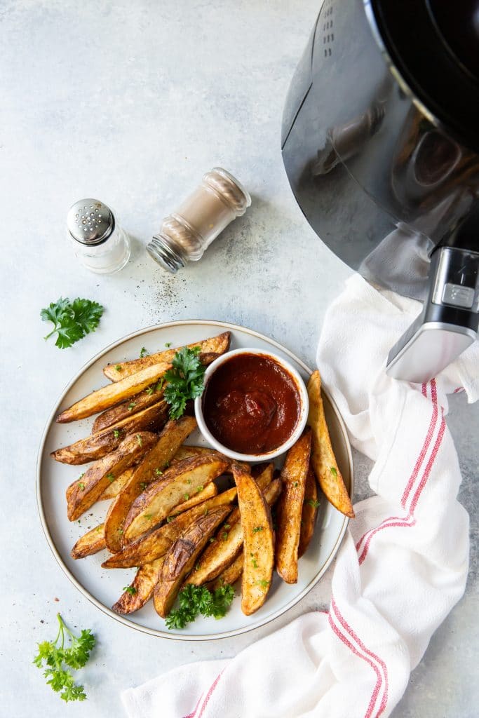 a plate of seasoned, cooked potato wedges with a side cup of ketchup.