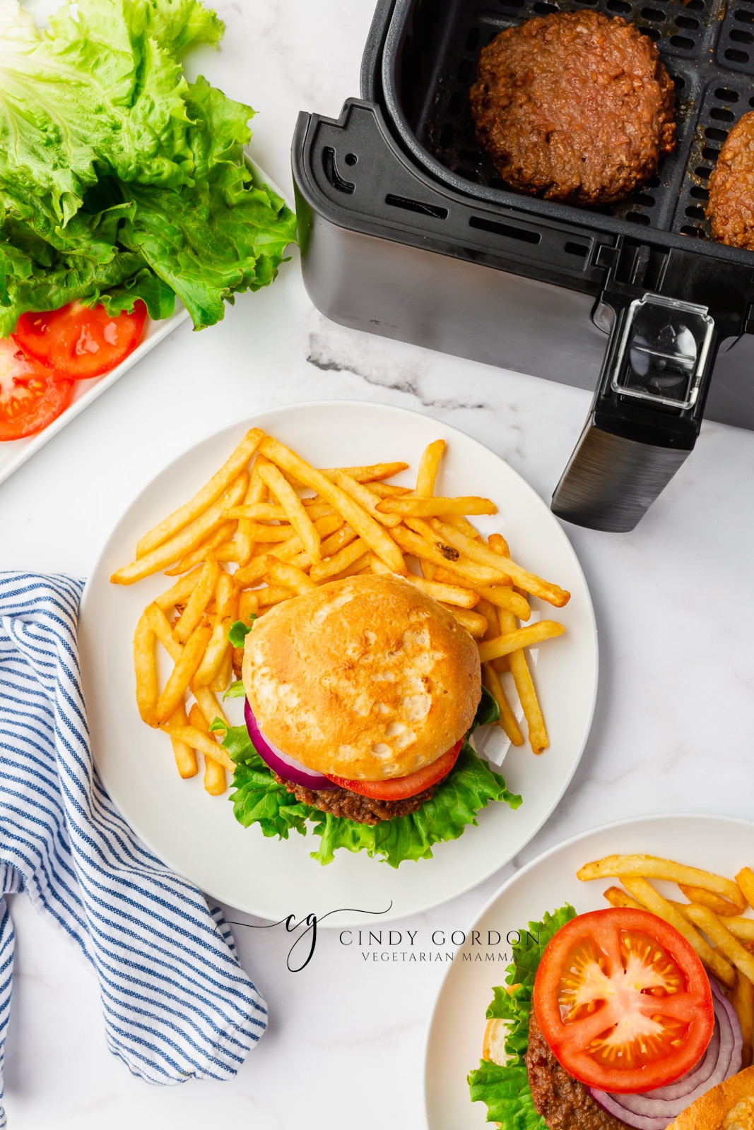 black air fryer basket. White plate with cooked fries and a bun with beyond burger air fryer with lettuce, tomato onion