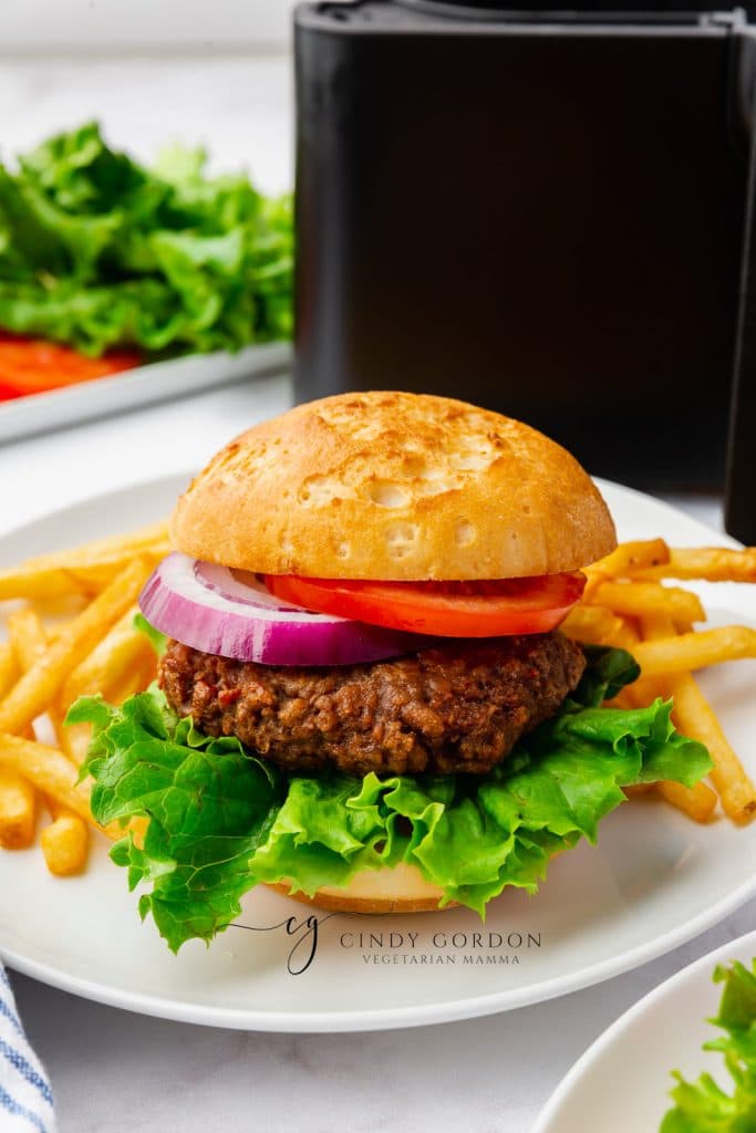 White plate with cooked fries and a bun with beyond burger air fryer with lettuce, tomato onion