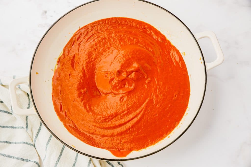 red smooth sauce in white enmanel skillet