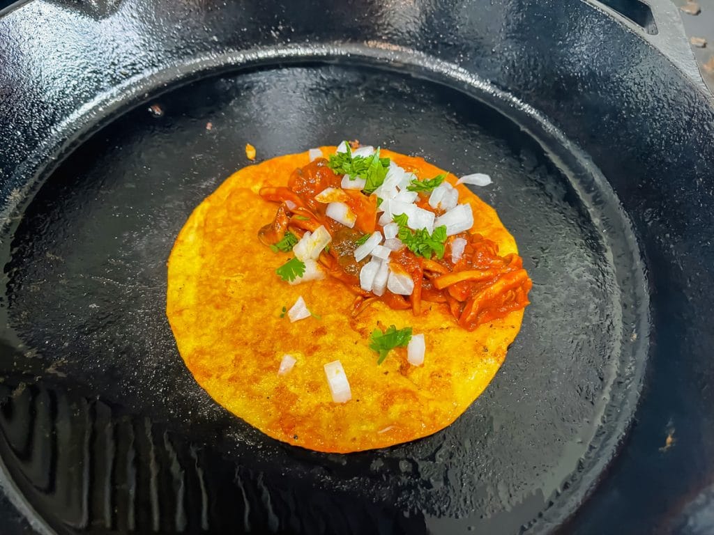 black cast iron skillet with brown tacos with red/brown mushrooms onion and green leaves
