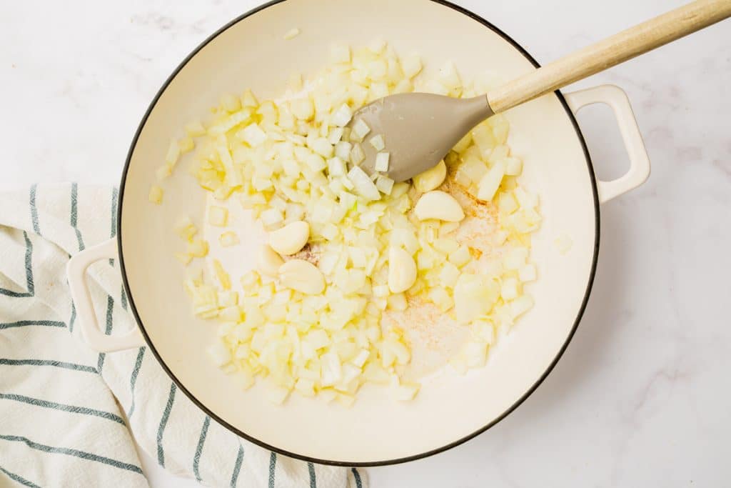 white skillet with spatula in it and onions an garlic cloves