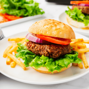 White plate with cooked fries and a bun with beyond burger air fryer with lettuce, tomato onion