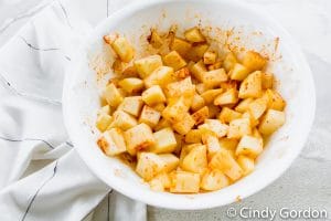 white bowl with raw cubed potatoes with oil and red seasoning on the cubes