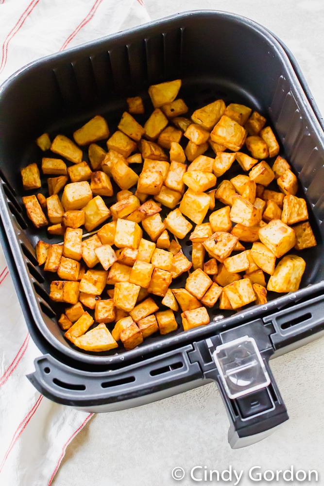 crispy brown cubed potatoes in a black air fryer basket