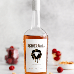 a bottle of screwball peanut butter whisky on a counter. Raspberries are in the background.