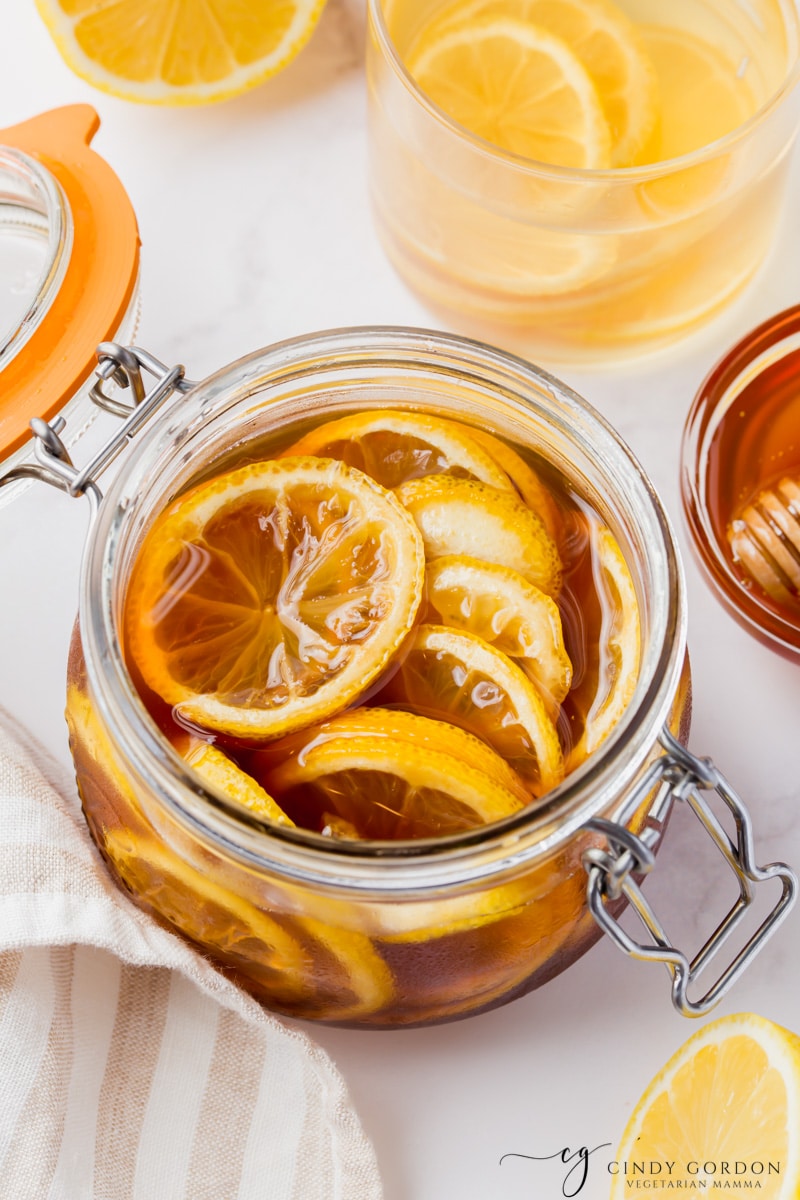 clear jar with lid. Inside are sliced lemons in brown dark honey. slices halved lemons on side and above and honey jar also visable