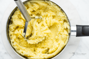 mashed potatoes with masher in a silver pot