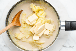 creamy off white liquid with butter slabs and mashed potatoes in a pot