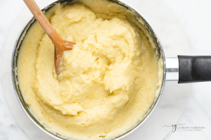 smooth mashed potatoes in silver pot with blank handle and wooden spoon