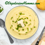 yellow whipped and smooth mashed potatoes with almond milk in a white bowl with two butter rectangles and green herbs on top