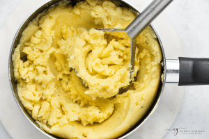 yellow mashed potatoes in a pot with a masher