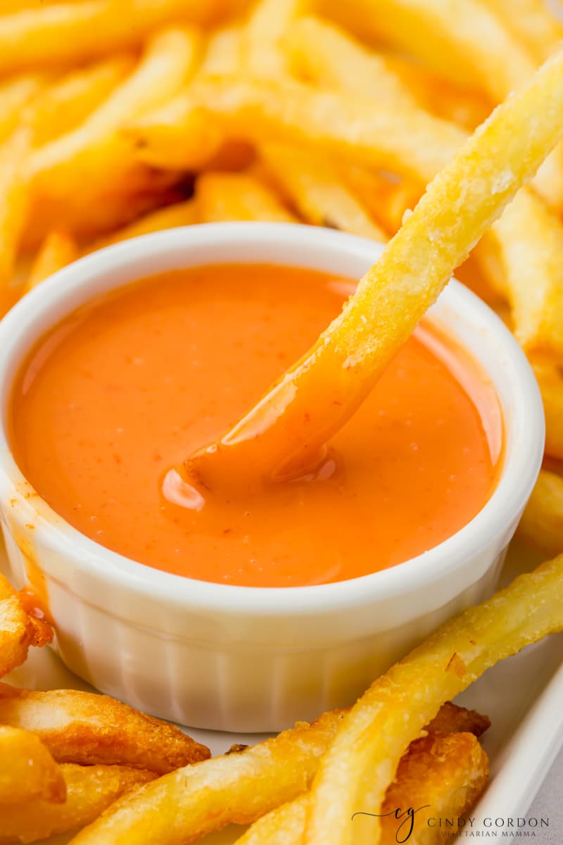upclose of Sweet and Spicy Sriracha Sauce in a white bowl with a fry being dipped in it
