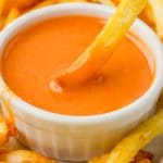 upclose of Sweet and Spicy Sriracha Sauce in a white bowl with a fry being dipped in it