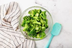 frozen green broccoli in glass bowl with salt and pepper on top with blue spoon to right side