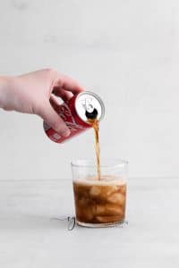 hand pouring coke into class with whiskey and ice cubes