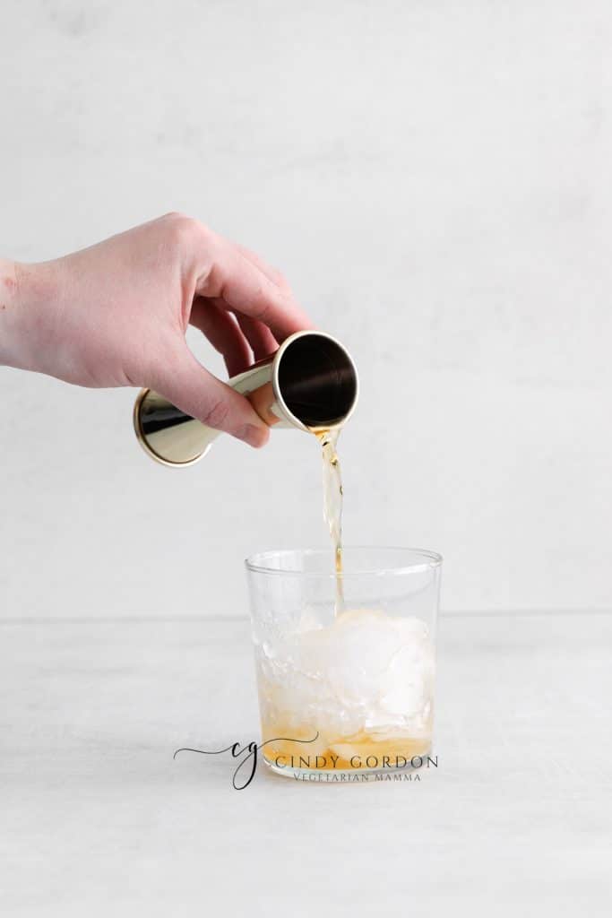 hand pouring whiskey into glass withe ice cubes