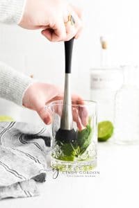 mint leaves and lime being hand muddled in short clear glass