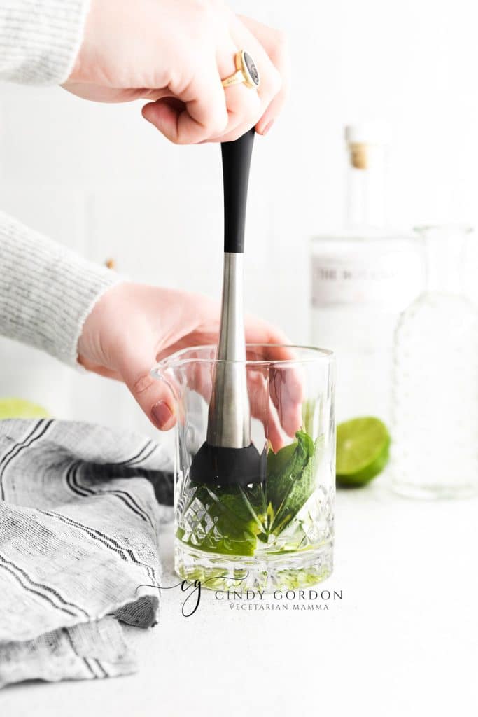 mint leaves and lime being hand muddled in short clear glass