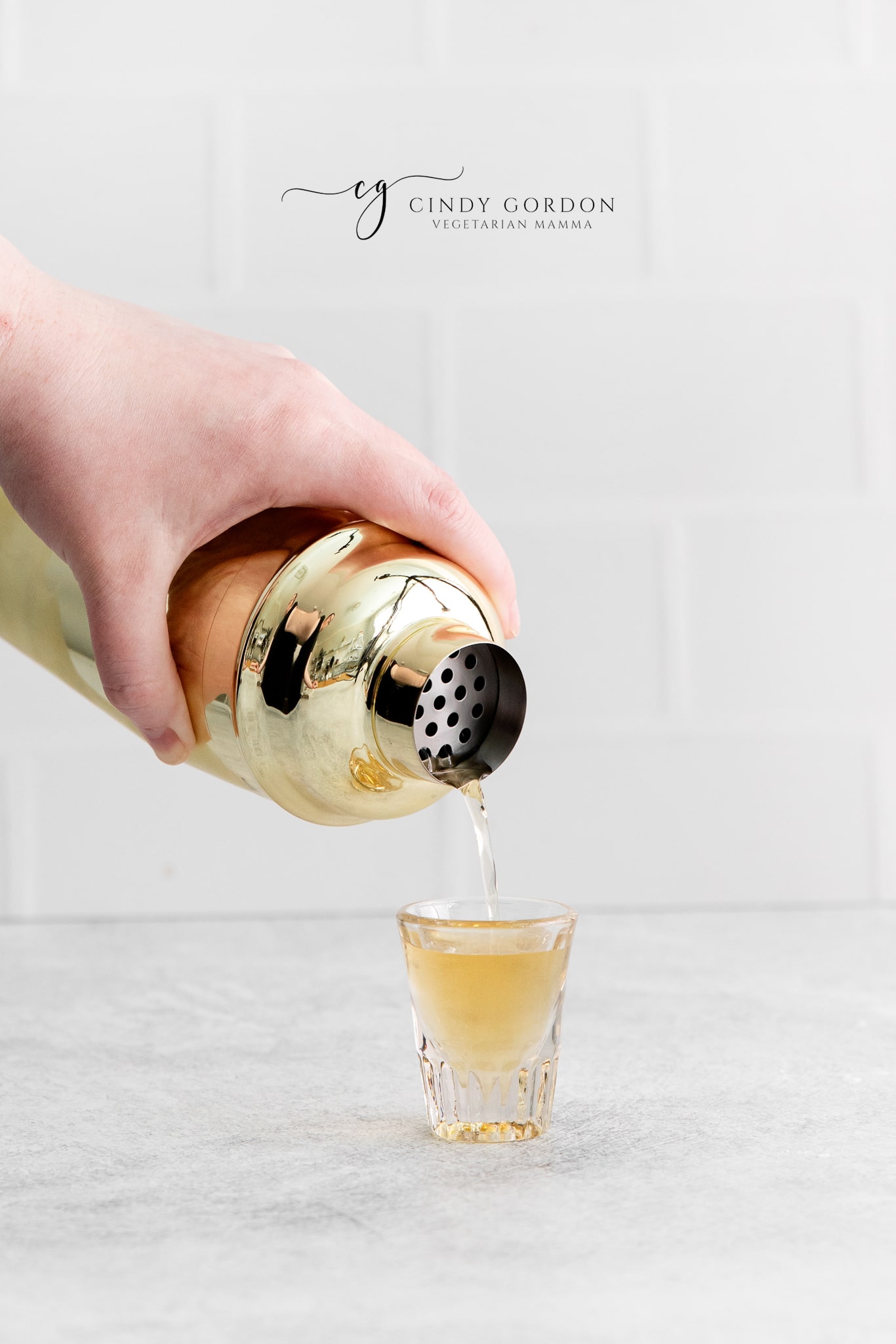 a shaker pouring a shot into a small shot glass.