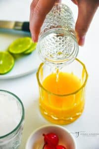 clear alcohol poured into a glass or orange pineapple juice.