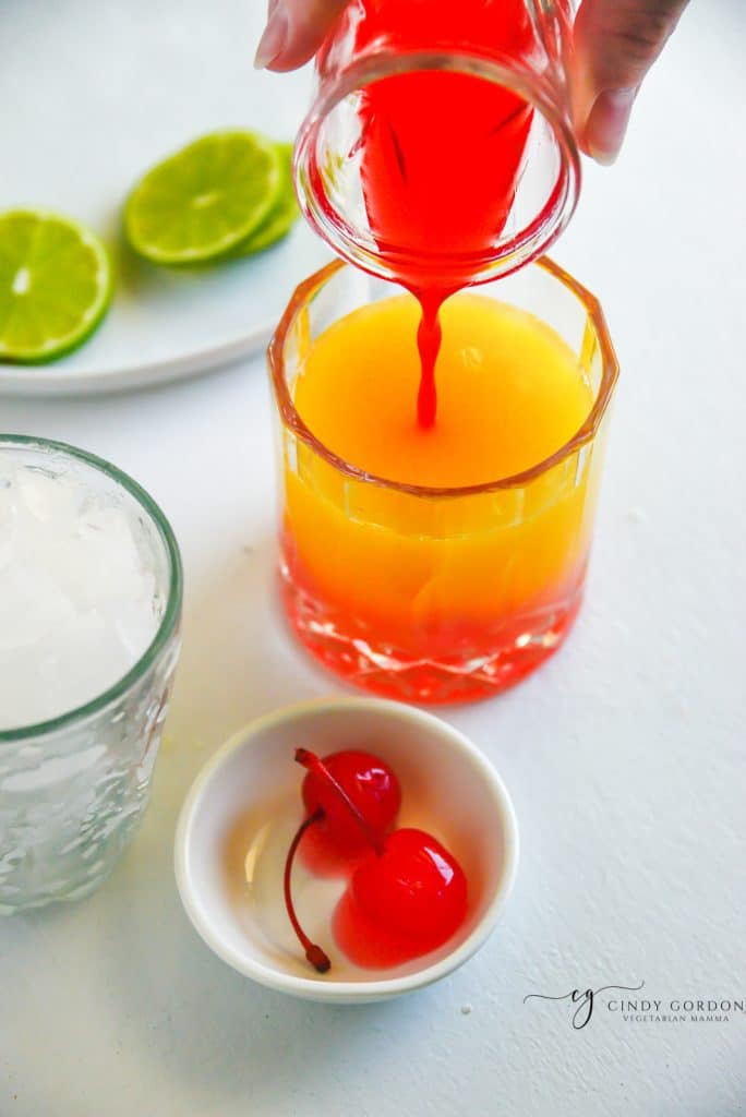 grenadine poured into a orange juice drink, sinking to the bottom.