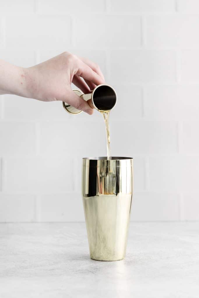 a jigger pouring a shot into a chilled cocktail shaker.