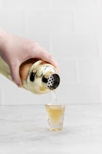 a shaker pouring a shot into a small shot glass.
