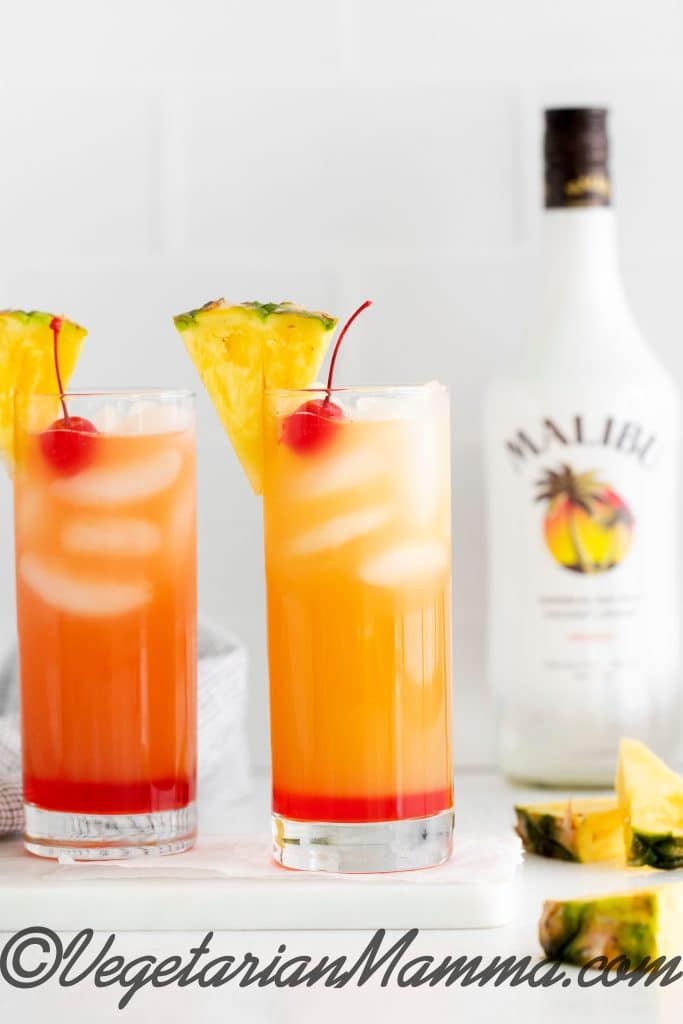 Two glasses with drink next to a bottle of Malibu rum.