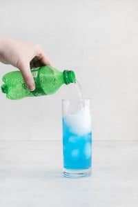 hand pouring sprite into tall glass with blue liquid