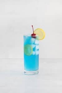blue motorcycle drink - blue liquid with white ice cubes in a tall clear glass. cherry and lemon wheel on top