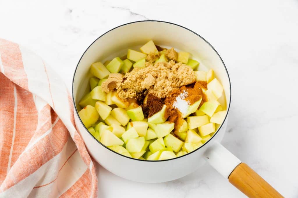 a white enameled saucepan filled with diced apples, spices, and brown sugar