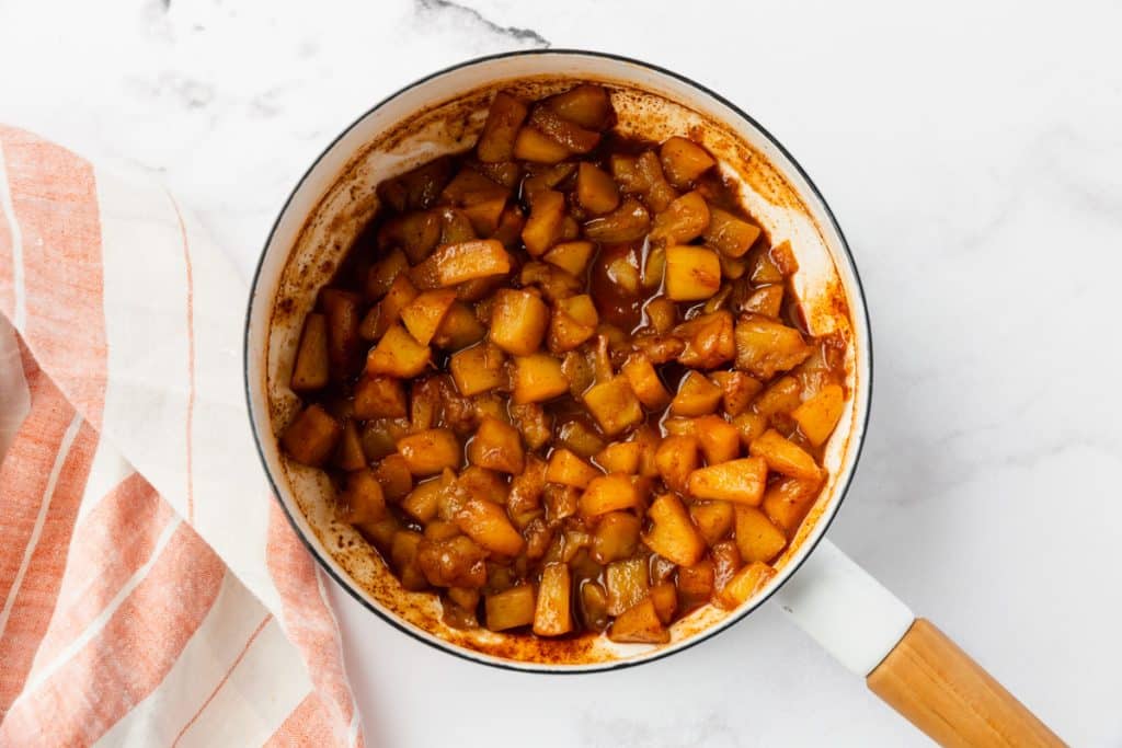 fully cooked apple compote in a white saucepan is deep brown.