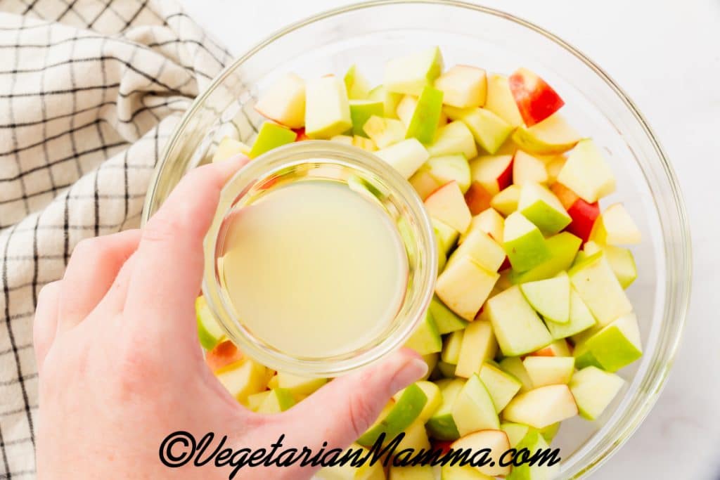 pouring lemon over chopped apples in a bowl.
