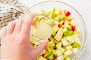 diced apples in a glass bowl with hand pouring lemon juice on top