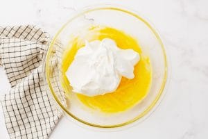 glass bowl with pudding (yellow) and cool whip on top with napkin to left
