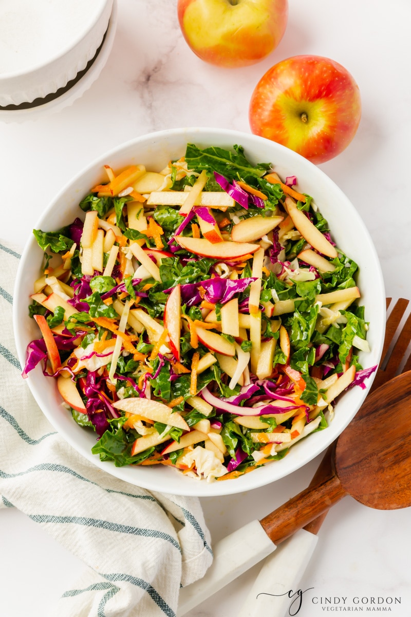 A white bowl of kale apple slaw with cabbage and shredded carrots, viewed from above