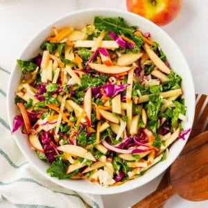 A white bowl of kale apple slaw with cabbage and shredded carrots, viewed from above