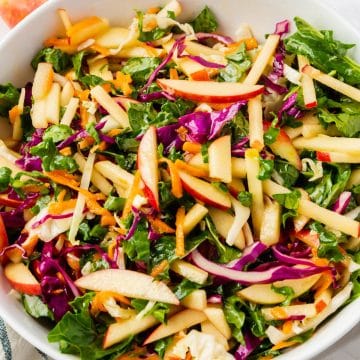 A white bowl of kale apple slaw with cabbage and shredded carrots, viewed from above