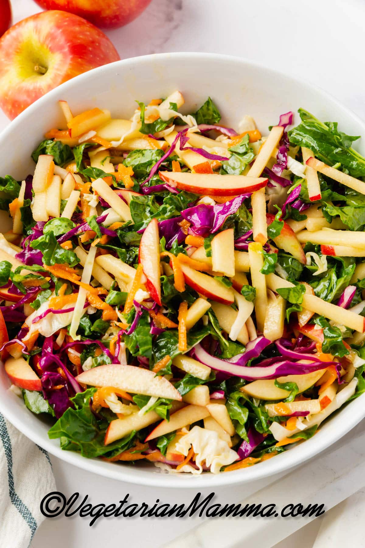 A white bowl of kale apple slaw with cabbage and shredded carrots, viewed from above