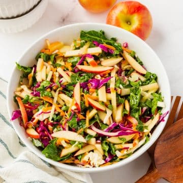 A white bowl of kale apple slaw with cabbage and shredded carrots.