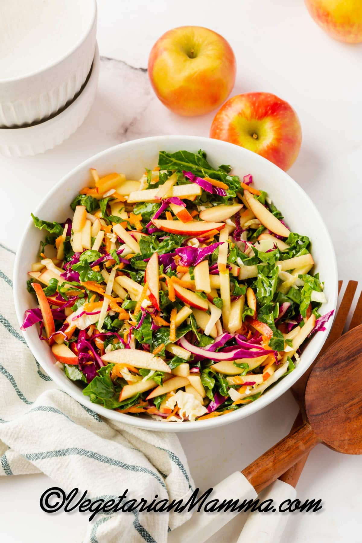 A white bowl of kale apple slaw with cabbage and shredded carrots, viewed from above