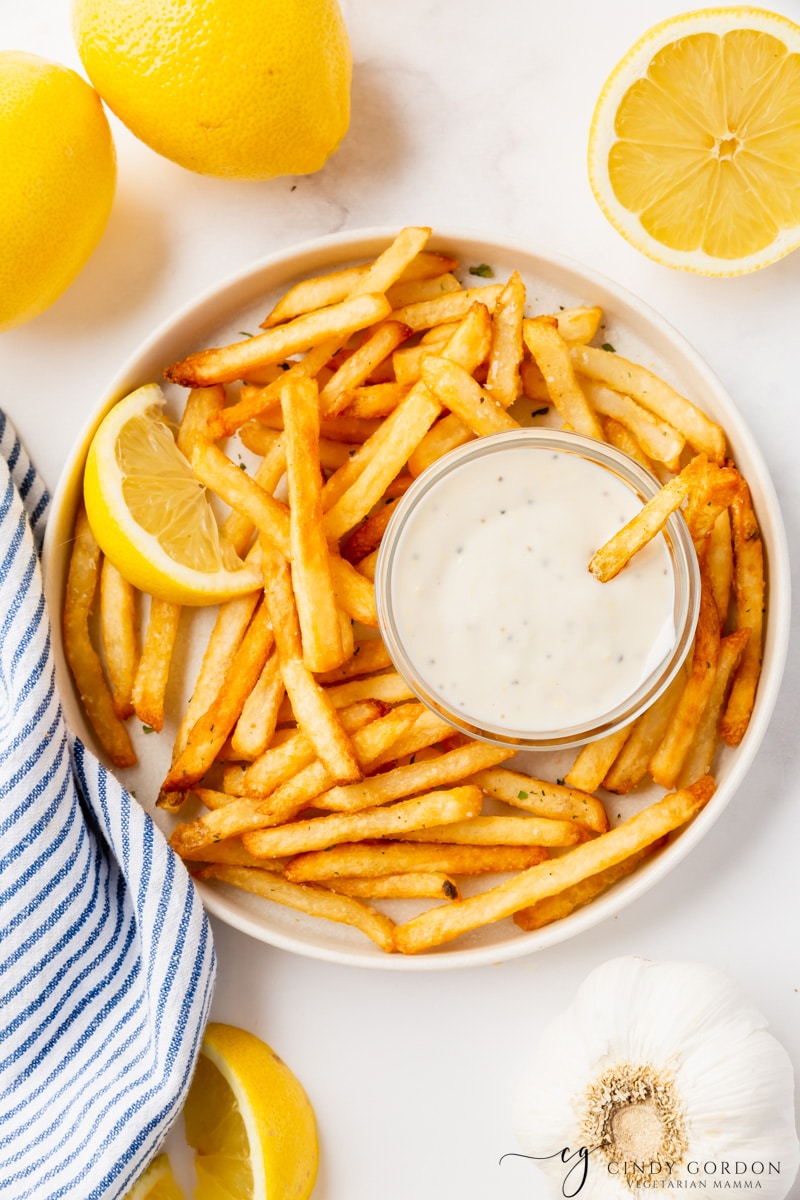 a plate of french fries with a cup of aioli in the middle.